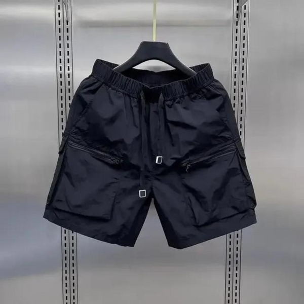 Zwarte cargoshorts met meerdere zakken, verstelbare tailleband en ritssluitingen, hangend aan een kledinghanger in een metalen kast.