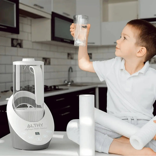 Jongen in moderne keuken met Althy waterfilter, houdt glas omhoog. Waterzuiveraar, keukenapparaat, gezond drinkwater, kindvriendelijk design.