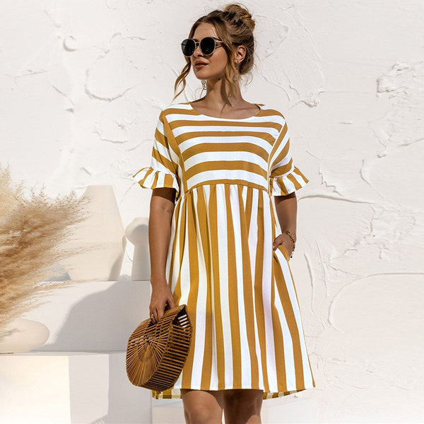 Vrouw in gestreepte zomerjurk met korte mouwen, zonnebril en rotan handtas. Perfecte outfit voor casual zomermode en stranduitjes.