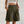 Vrouw draagt olijfgroene, hoge taille bermuda shorts met plooien en knopen, gecombineerd met een witte crop top. Trendy damesmode zomeroutfit.