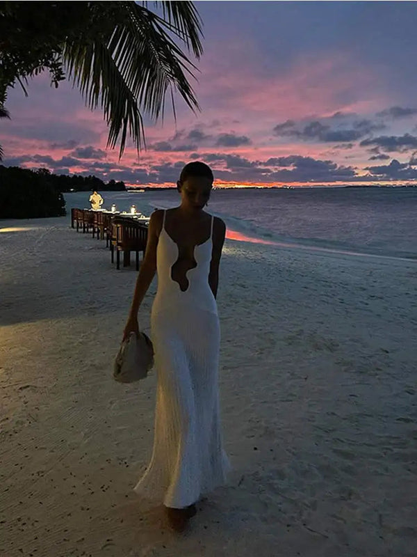 Vrouw in elegante witte jurk loopt op tropisch strand bij zonsondergang, palmbomen en zee op achtergrond. Perfecte vakantiebestemming, romantische sfeer.