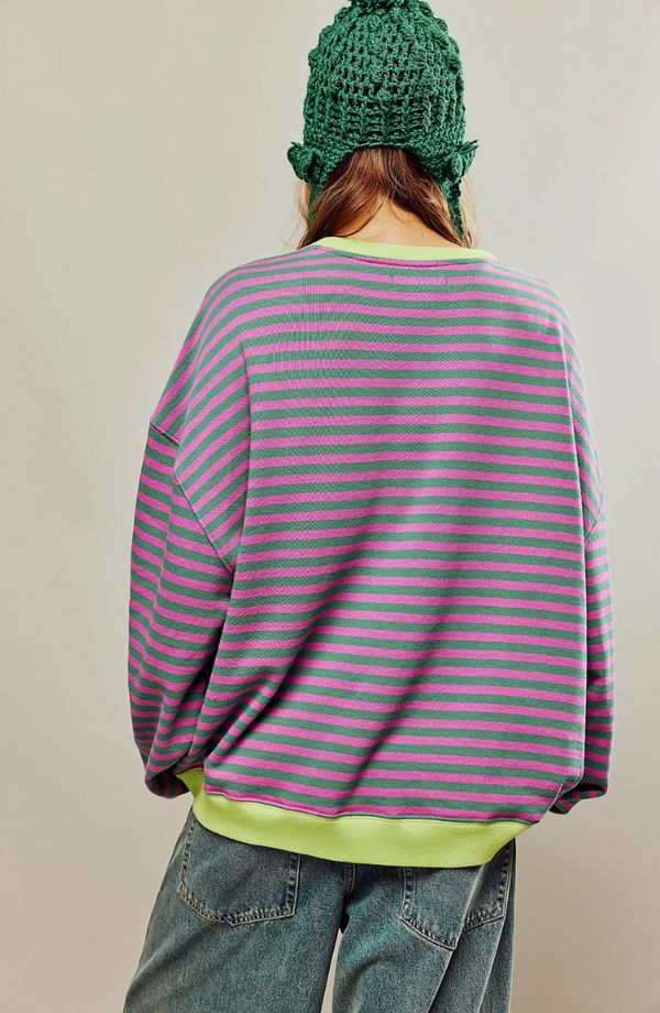 Vrouw in gestreepte trui met roze en groene strepen, groene gebreide muts, blauwe jeans. Modieuze casual outfit, herfstkleding.