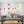 Grijze bank met kleurrijke kussens, grote rode wandklok en abstract schilderij in moderne woonkamer. Stijlvol interieurontwerp, Scandinavische stijl.