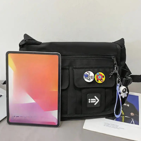 Zwarte schoudertas met kleurrijke buttons en sleutelhanger, naast een tablet met oranje scherm. Ideaal voor dagelijks gebruik en tech-liefhebbers.