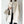 Dame in elegante witte mantel met parelknopen, grijze coltrui en stijlvolle beige handtas. Modieuze winteroutfit, minimalistisch design.