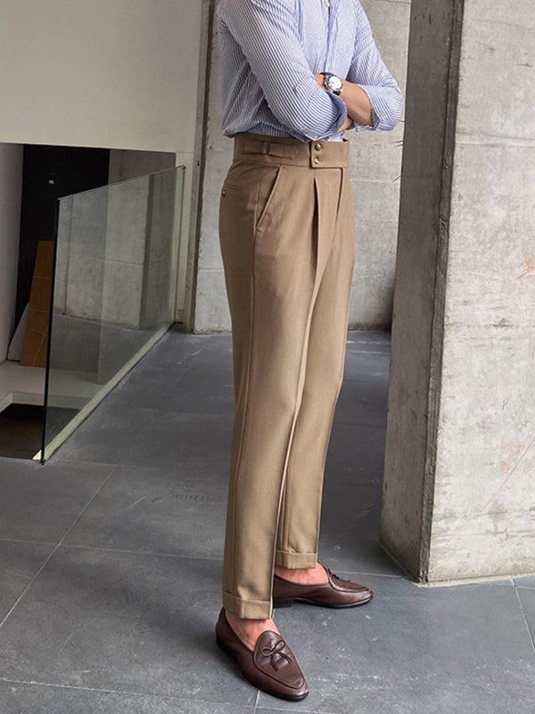 Man in beige pantalon en bruine loafers, gekruiste armen, gestreept overhemd, moderne betonnen omgeving. Stijlvolle herenmode, zakelijke casual look.