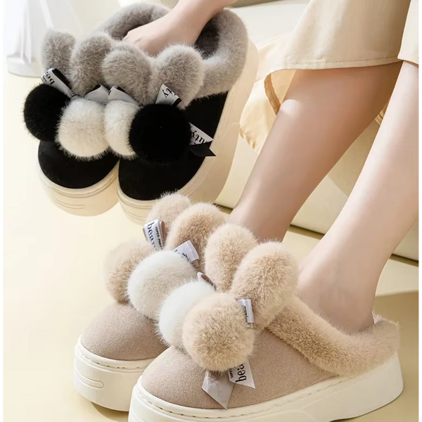 Pluche pantoffels met dikke zolen, pompons en strikjes in beige en zwart. Comfortabele wintermode, warme damespantoffels, trendy huisstijl.