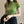 Vrouw in groene coltrui met korte mouwen, zwarte rok en horloge, houdt zwarte trui vast. Stijlvolle damesmode, casual chique outfit.