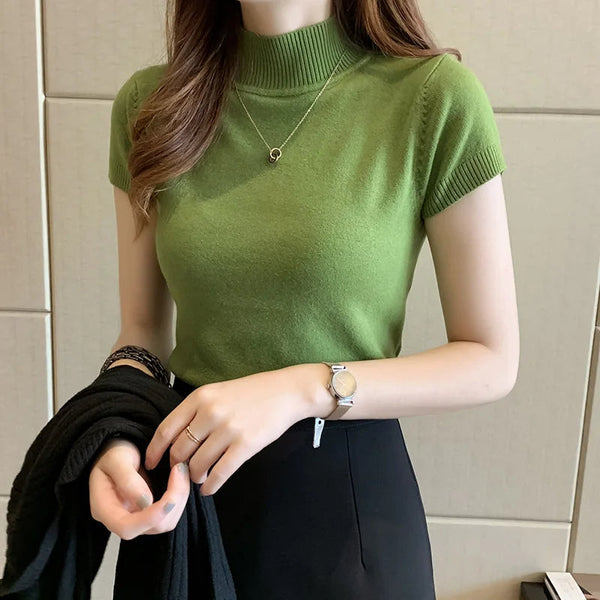 Vrouw in groene coltrui met korte mouwen, zwarte rok en horloge, houdt zwarte trui vast. Stijlvolle damesmode, casual chique outfit.