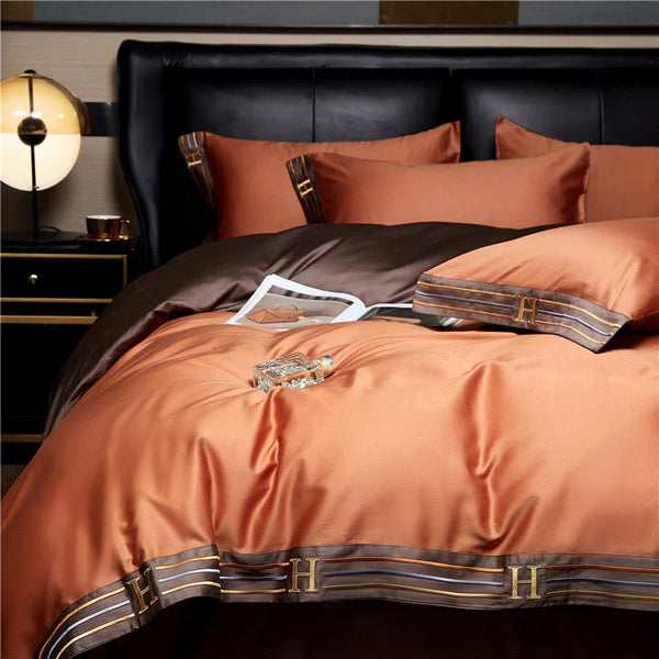 Luxe oranje en bruine satijnen dekbedovertrekset met initialen "H", inclusief kussenslopen en bedlamp, perfect voor moderne slaapkamerinrichting.