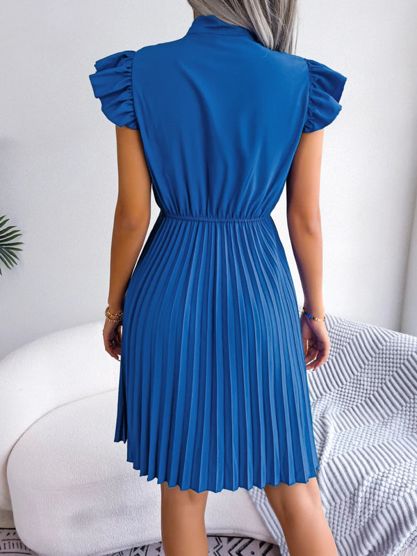 Blauwe geplooide jurk met korte mouwen, gedragen door vrouw, rugaanzicht. Elegante damesmode, zomerjurk, casual stijl, comfortabele pasvorm.