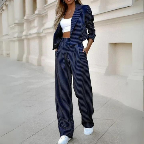 Vrouw in blauw-wit gestreept pak met crop top en sneakers, modieuze zakelijke outfit, stedelijke achtergrond, trendy dameskleding.