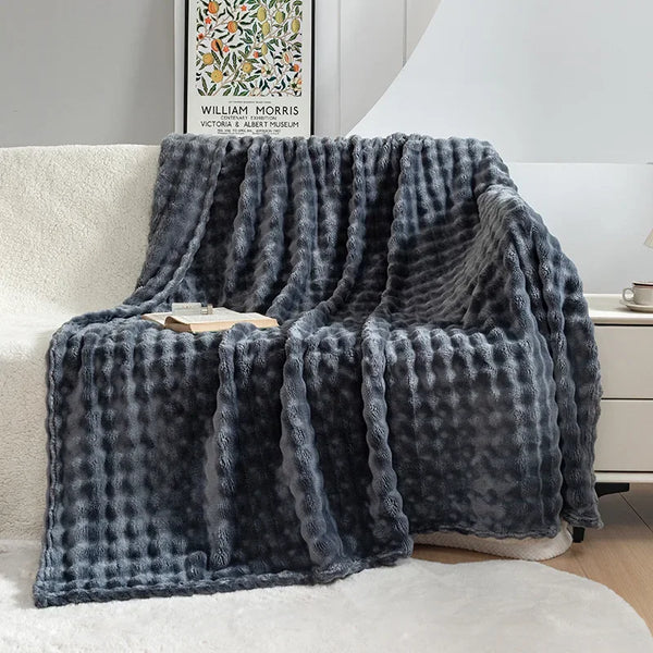Grijze, zachte, gewafelde fleece deken op een bank in een moderne woonkamer, naast een boek en een kopje thee. Perfect voor gezellige winteravonden.