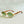 Gouden ronde zonnebril met groene glazen en houten pootjes op grijze achtergrond. Stijlvolle unisex zonnebril, vintage design, modieuze accessoires.