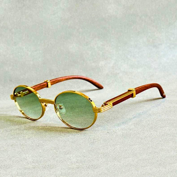Gouden ronde zonnebril met groene glazen en houten pootjes op grijze achtergrond. Stijlvolle unisex zonnebril, vintage design, modieuze accessoires.
