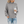 Vrouw in grijze gebreide trui met col, houdt een kartonnen koffiebeker vast, draagt gescheurde blauwe jeans. Casual herfstmode.