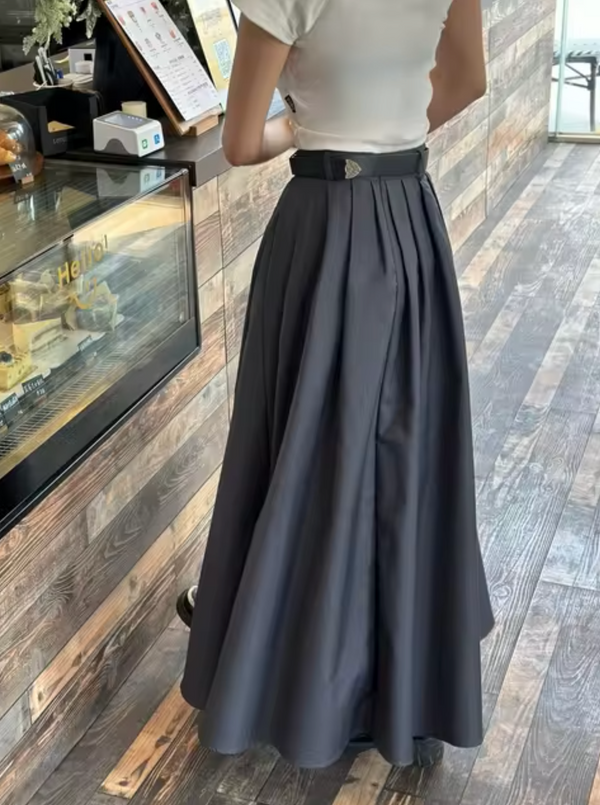 Vrouw in lange, zwarte plooirok bij houten toonbank in café. Stijlvolle mode, casual outfit, trendy rok, moderne kleding, winkelinterieur.