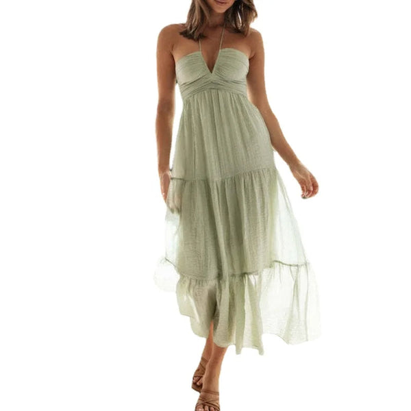 Vrouw in lichtgroene zomerjurk met halternek en gelaagde rok, perfect voor casual en strandmode. Elegante en luchtige dameskleding.