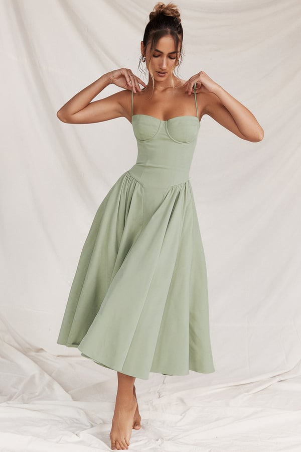 Vrouw in elegante, lichtgroene midi-jurk met spaghettibandjes, staand op witte achtergrond. Perfect voor zomer- of cocktailfeesten.