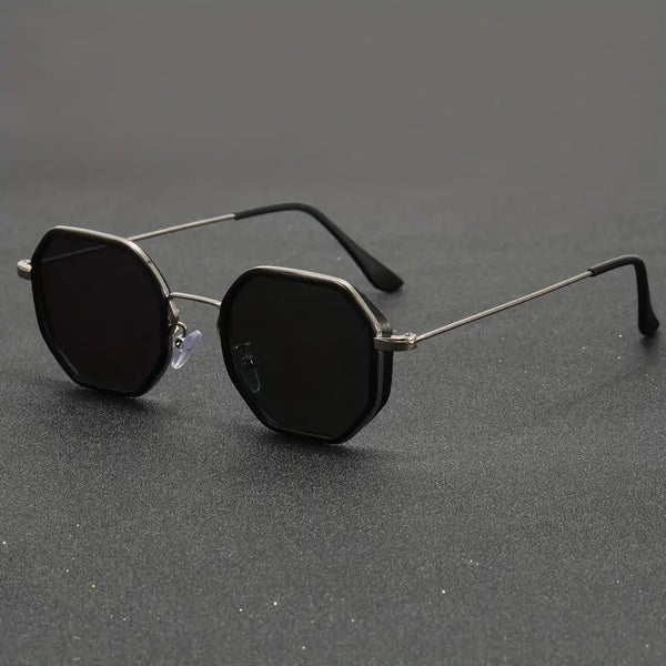 Zwarte achthoekige zonnebril met metalen montuur op grijze achtergrond, modieuze unisex zonnebril, UV-bescherming, trendy accessoire.