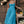 Jonge vrouw in blauwe zomerjurk met mand vol groenten en fruit, leunend tegen houten schuur. Bohemian mode, landelijke stijl, zomerse outfit.