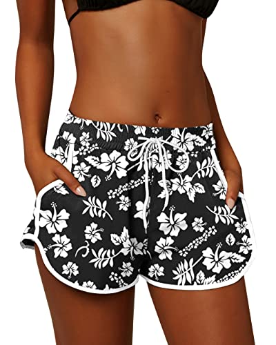 Vrouw draagt zwarte sportshort met witte bloemenprint, elastische tailleband en trekkoord. Perfect voor zomerse activiteiten en strandmode.