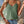 Vrouw in groene kanten top en denim shorts, met witte schoudertas en sieraden, buiten in zomerse setting. Trendy damesmode, casual outfit.
