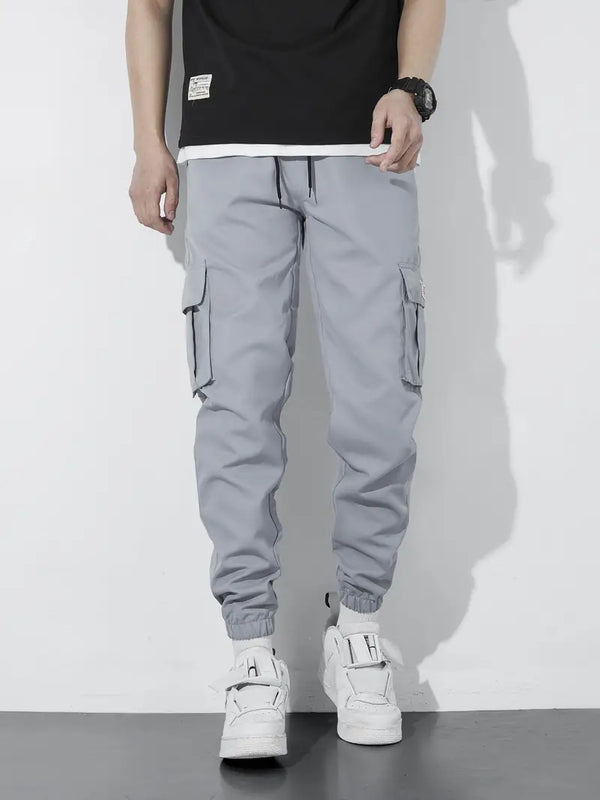Grijze cargobroek voor heren met zakken, casual streetwear stijl, gecombineerd met witte sneakers. Comfortabele en modieuze herenkleding.