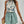 Vrouw in zomerse outfit met bloemen top en mintgroene shorts, draagt een strohoed en rotan tas. Perfecte look voor strandvakantie of zomerse dag.