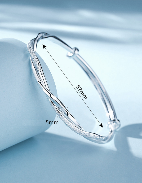 Zilveren armband met gedraaide details, diameter 57mm, breedte 5mm, op blauwe achtergrond. Elegante sieraden, modieuze accessoires.
