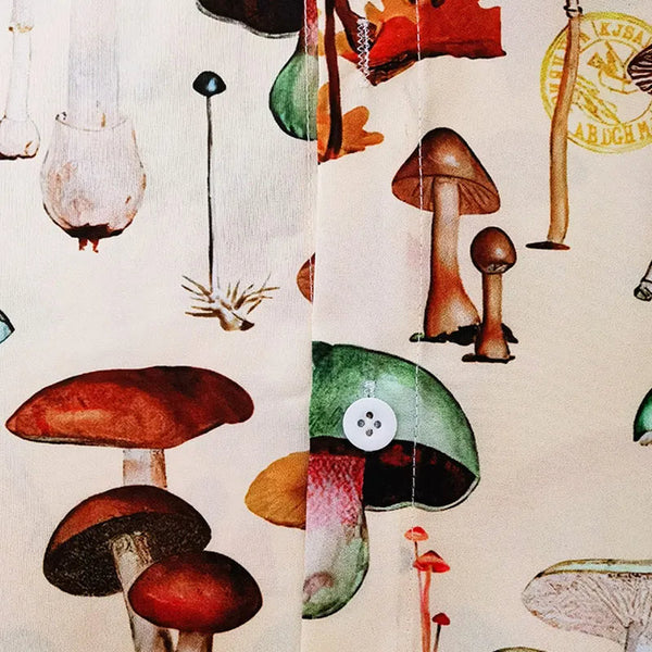 Afbeelding van een kleurrijk overhemd met paddenstoelenprint, inclusief diverse soorten paddenstoelen op een beige achtergrond, knoop zichtbaar.