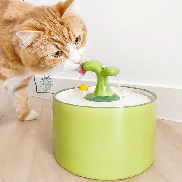 Oranje kat drinkt uit groene kattenfontein met bloemvormig ontwerp, ideaal voor huisdieren. Hydratatie, huisdieraccessoires, kattenverzorging.
