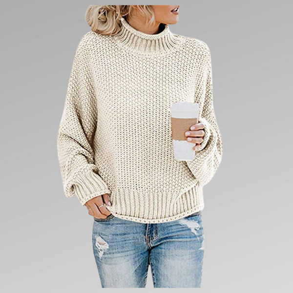 Vrouw in crèmekleurige gebreide trui met opgerolde mouwen, houdt een kartonnen koffiebeker vast, draagt gescheurde blauwe jeans. Casual herfstmode.