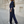 Vrouw in blauw gestreept pak met lange broek en jasje, witte sneakers, staand op trottoir voor klassieke architectuur. Modieuze dameskleding.