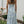Vrouw in lange, blauwe bloemenjurk met blote rug, staand in tuin naast tafel met rozen. Zomermode, elegante dameskleding, buitenstijl.