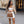 Vrouw in modieuze outfit met bruine handtas, witte rok en beige jas, poseert voor luxe winkel. Stijlvolle straatmode, stedelijke achtergrond.