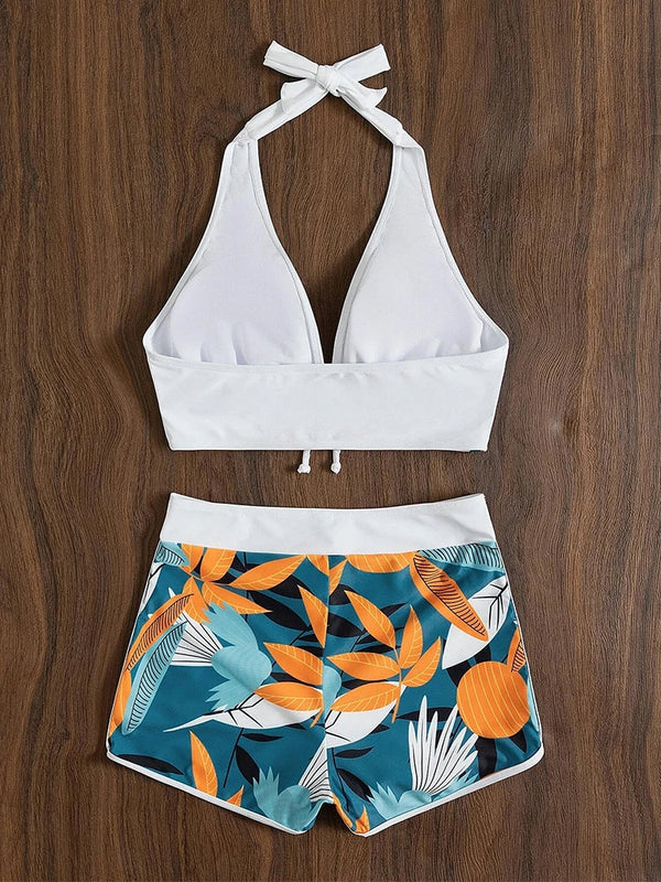 Witte halterbikini met tropische bladerenprint op short, houten achtergrond. Perfect voor strandmode, zomeroutfit, dames zwemkleding.
