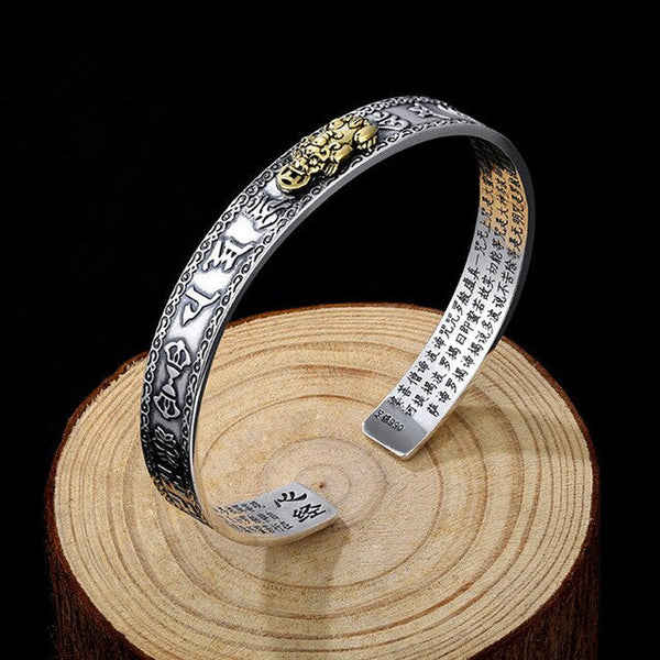 Zilveren armband met gouden draak en Chinese karakters, rustend op houten schijf. Luxe sieraden, oosterse stijl, handgemaakt ontwerp.