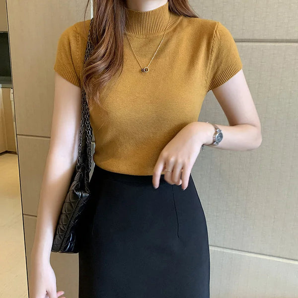 Vrouw in mosterdgele trui en zwarte rok, draagt een zwarte schoudertas en zilveren horloge. Stijlvolle damesmode, casual chique outfit.