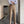 Stijlvolle man in beige pantalon en gestreept overhemd, leunend tegen een betonnen pilaar. Modieuze bruine loafers. Moderne herenmode, casual chic.