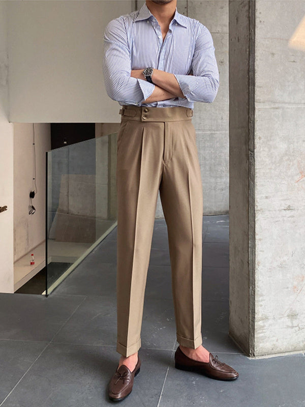 Stijlvolle man in beige pantalon en gestreept overhemd, leunend tegen een betonnen pilaar. Modieuze bruine loafers. Moderne herenmode, casual chic.