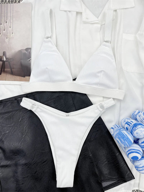 Witte ribgebreide bikini set op zwarte leren rok, naast blauw-witte marmeren kaarsen en een wit overhemd. Perfect voor zomer- en strandmode.