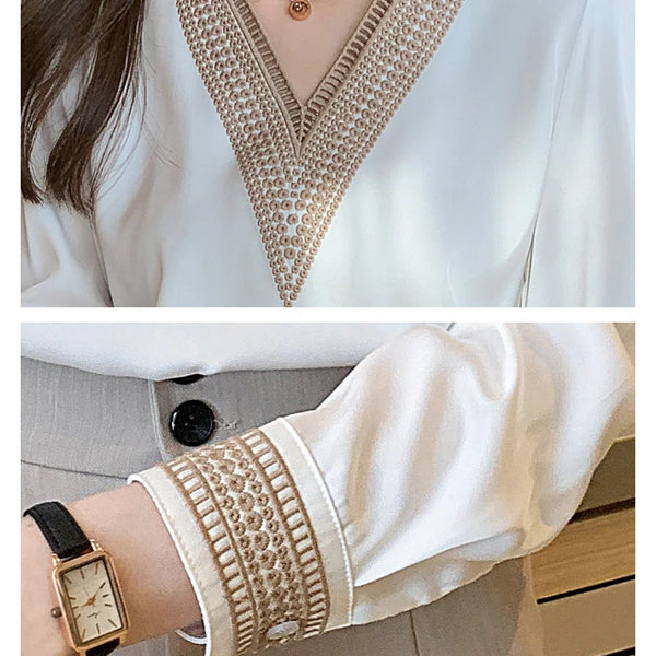Witte blouse met V-hals en beige borduursel, gecombineerd met een horloge en grijze broek. Elegante damesmode, stijlvolle blouse details.