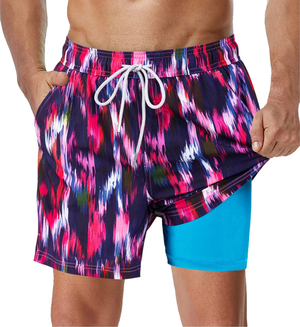 Man in kleurrijke zwemshorts met abstract patroon en blauwe onderlaag, handen in zakken. Modieuze strandkleding voor heren, zomerstijl.