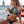 Vrouw in groene bikini drinkt cocktail op strand, met zee en lantaarns op achtergrond. Zomerse strandmode, vakantie, tropische sfeer.