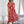 Vrouw in elegante rode jurk met witte bloemenprint, staand in moderne woonkamer. Trendy damesmode, zomerjurk, casual chique stijl.