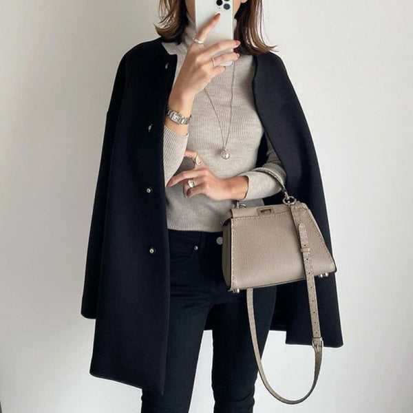 Vrouw in stijlvolle herfstoutfit met zwarte jas, grijze trui en beige handtas. Modieuze dameskleding, herfstmode, casual chic look.