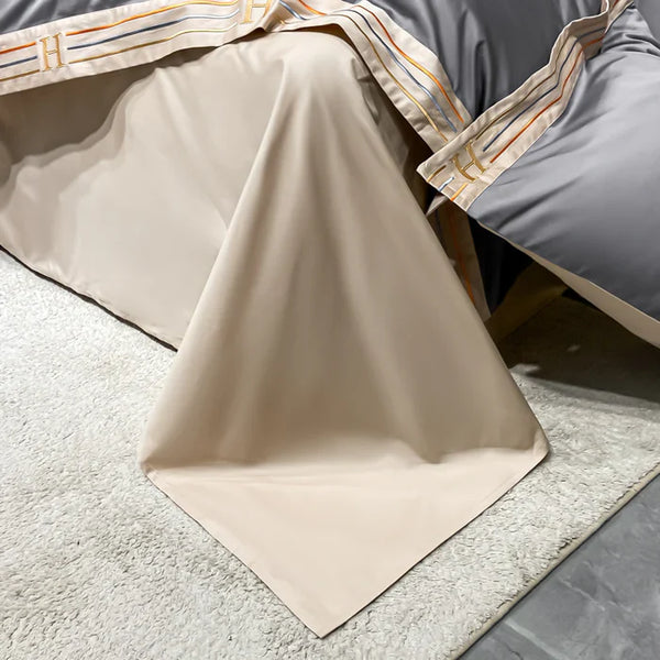 Luxe beige beddengoed set met grijze en gestreepte accenten, elegant gedrapeerd over een bed op een zachte, witte vloerkleed. Perfect voor moderne slaapkamers.