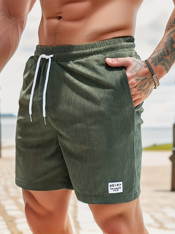 Groene corduroy zwembroek voor heren met witte trekkoorden, gedragen door een getatoeëerde man op het strand. Comfortabele en stijlvolle strandkleding.