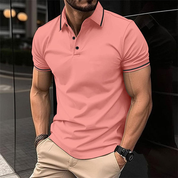 Man in roze poloshirt met korte mouwen en beige broek, staand buiten bij een glazen gebouw. Modieuze herenkleding, casual stijl.